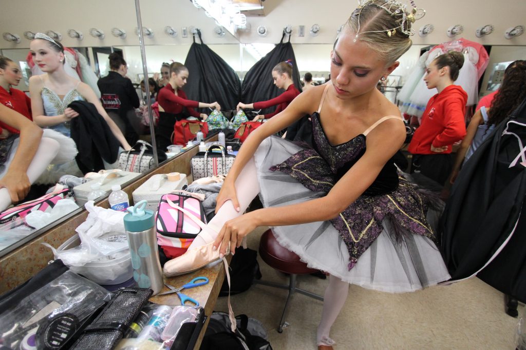 A young ballerina taking off her slipper.