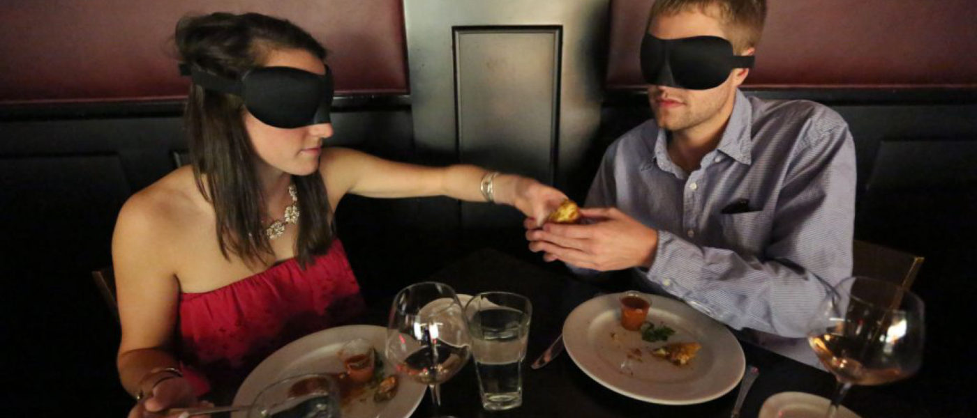 A blind-folded couple enjoying dinner.