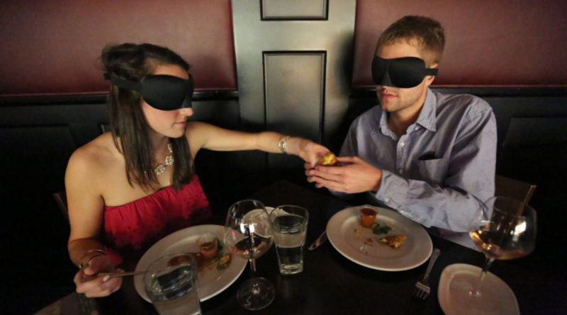 A blind-folded couple enjoying dinner.