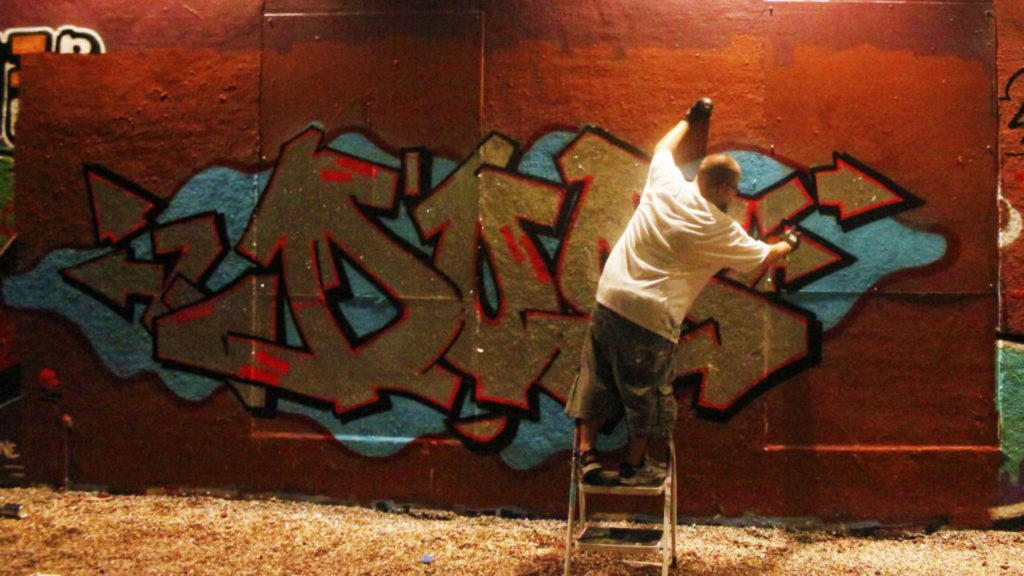 Graphic artist known as Colerizm spraying his tag on a wall.