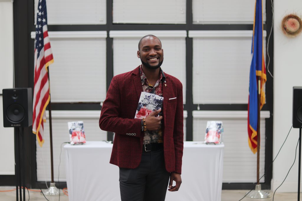 Haitian author David Frederick posing for the camera with his book.