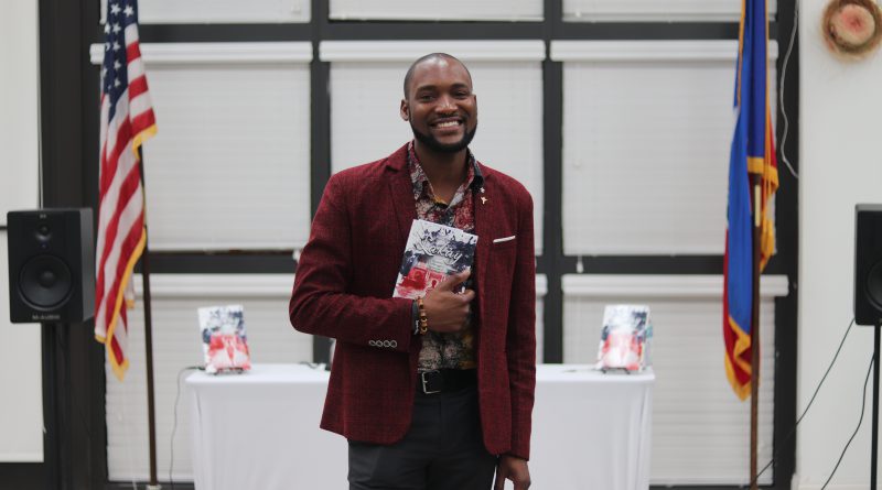 Haitian author David Frederick posing for the camera with his book.